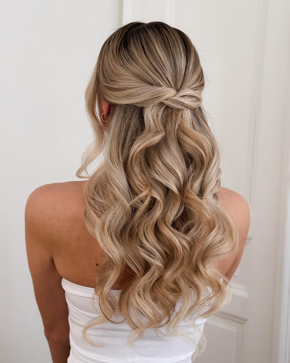 Blonde wavy hair styled half up half down with a small knot back