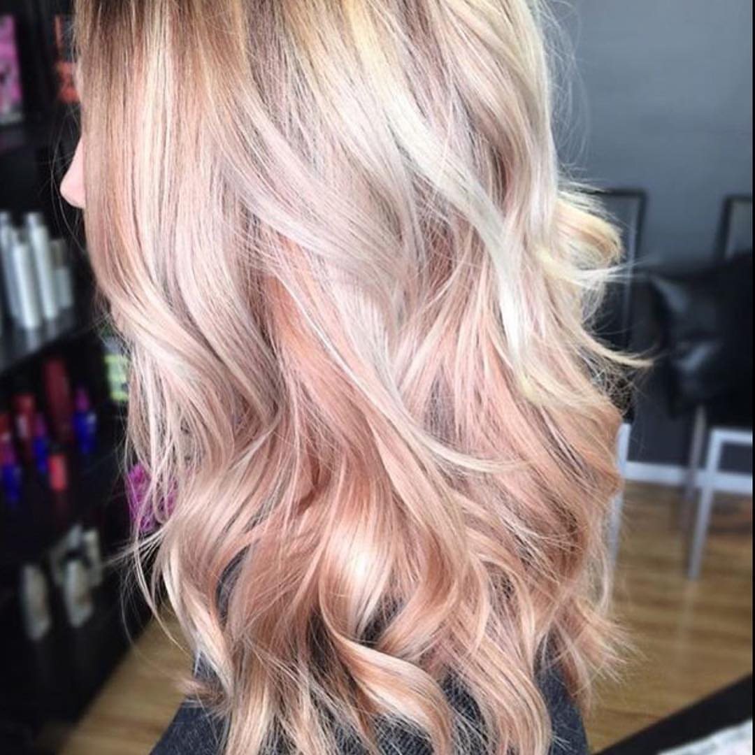 Wavy blonde hair with soft rose gold highlights styled in loose curls.