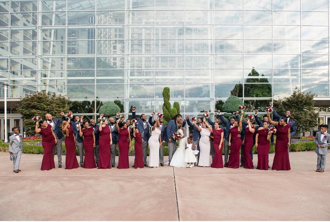 Wedding party in burgundy dresses and navy suits posing in front of a glass building.