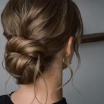 A woman with light brown hair styled in a textured low bun updo.