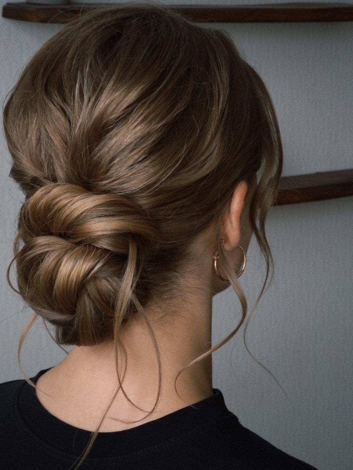 A woman with light brown hair styled in a textured low bun updo.