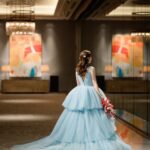 Woman in a voluminous light blue tiered tulle gown standing in a luxury room.