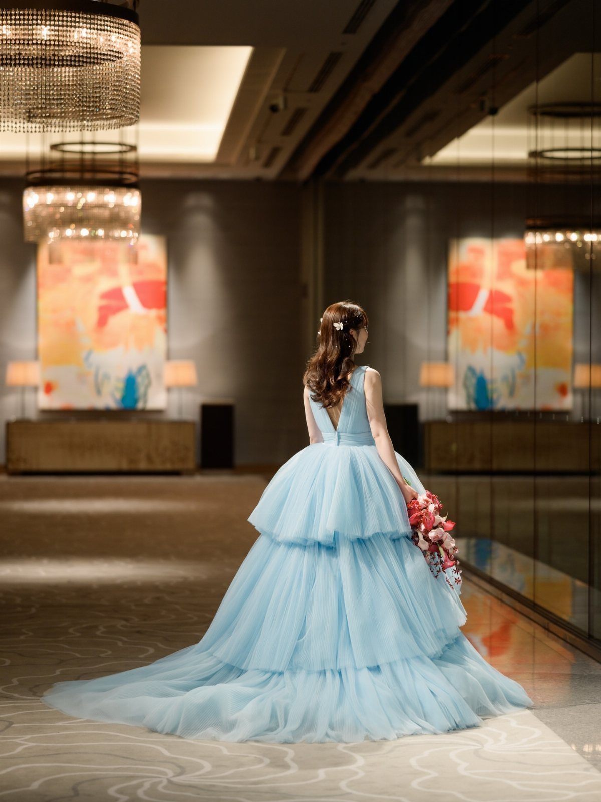 Woman in a voluminous light blue tiered tulle gown standing in a luxury room.