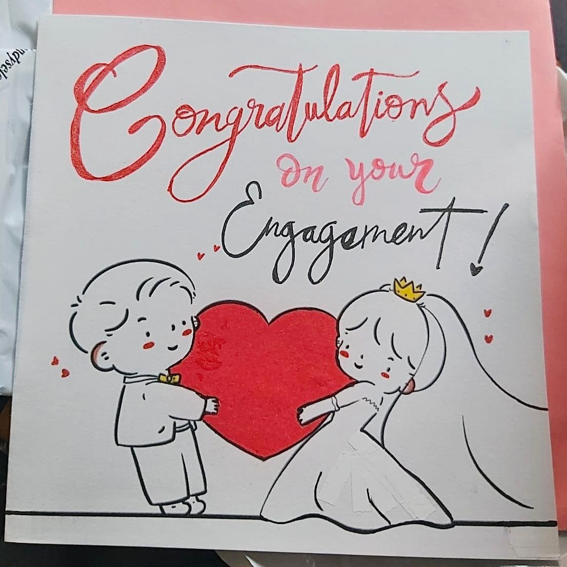 Handmade engagement card with a cartoon couple holding a large red heart.
