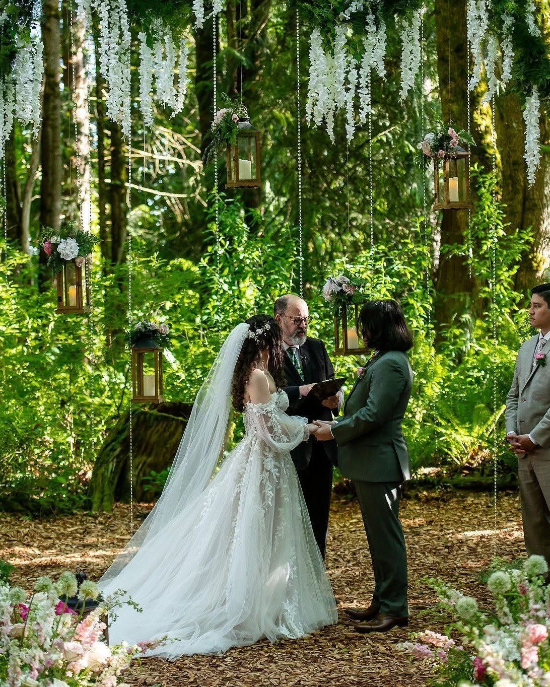 A bride and groom exchanging vows in a forest decorated with hanging lanterns and wisteria.