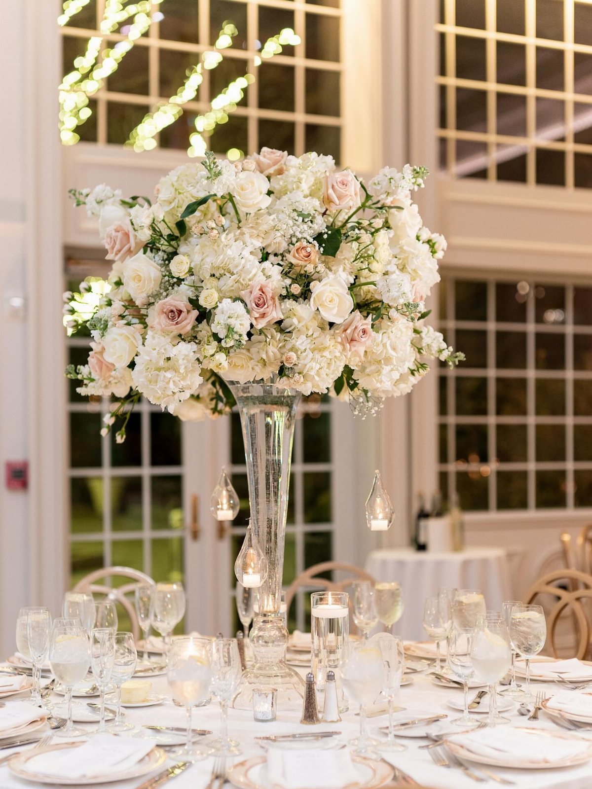 Large white and pink floral centerpiece in a tall glass vase on a formal wedding table.