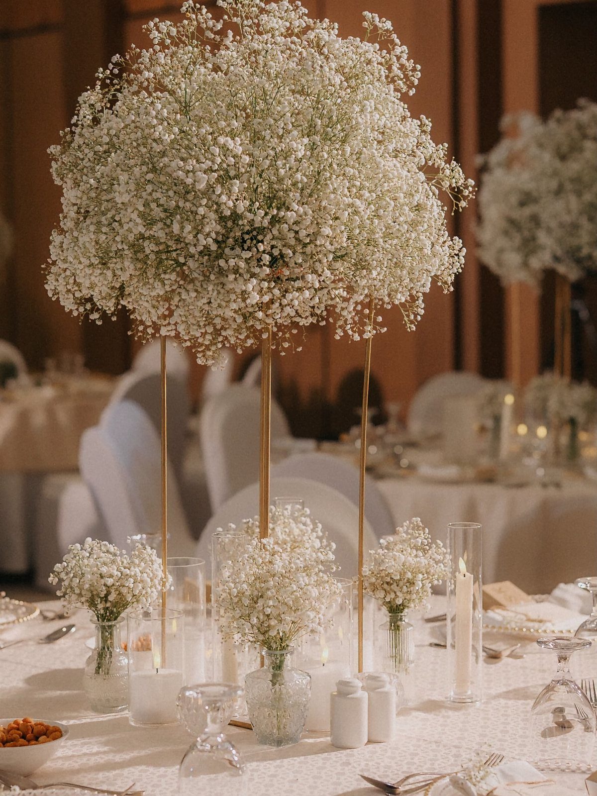 Tall white baby's breath floral centerpiece on a wedding reception table with candles.