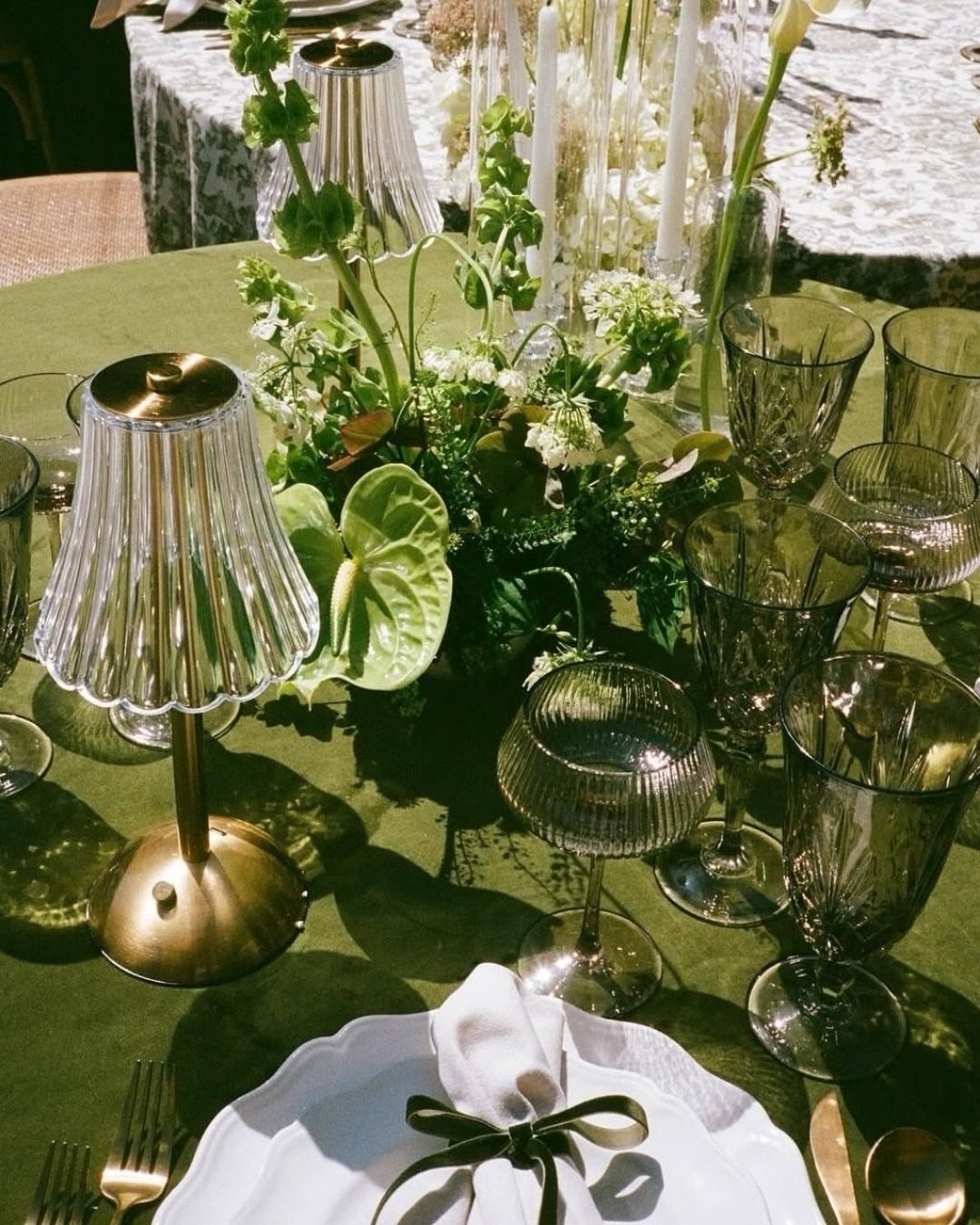 A wedding table set with forest green linens, dark glassware, and white floral arrangements.