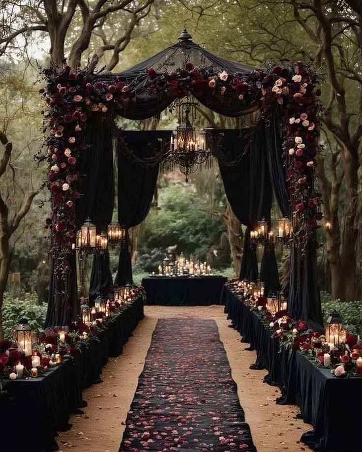 Gothic wedding altar with black drapery, red roses, and candles in a forest setting.