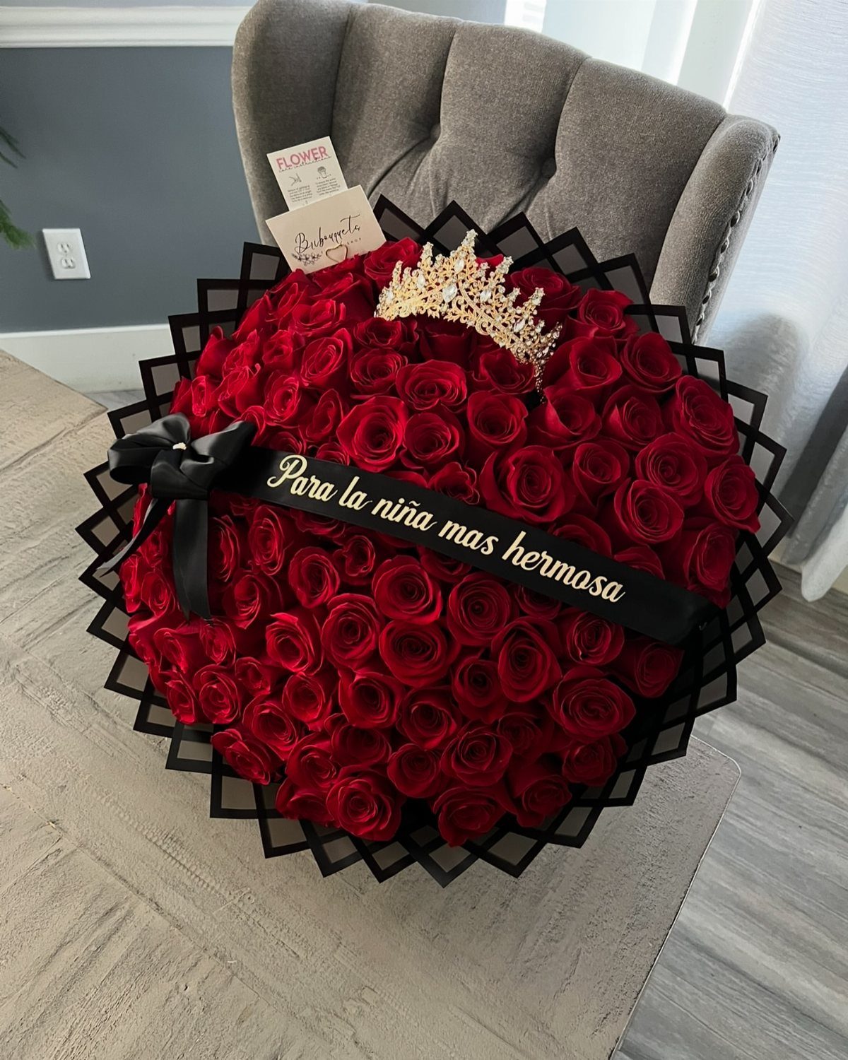 Large round bouquet of red roses with a gold tiara and black ribbon.