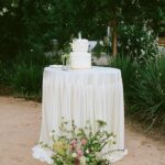 Ivory tablecloth on a round table with a white wedding cake and flowers