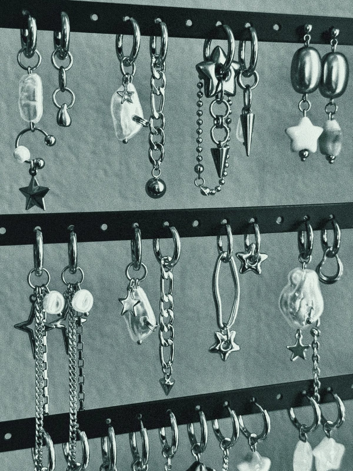 Silver metal earrings with star and pearl charms hanging on a black display board.
