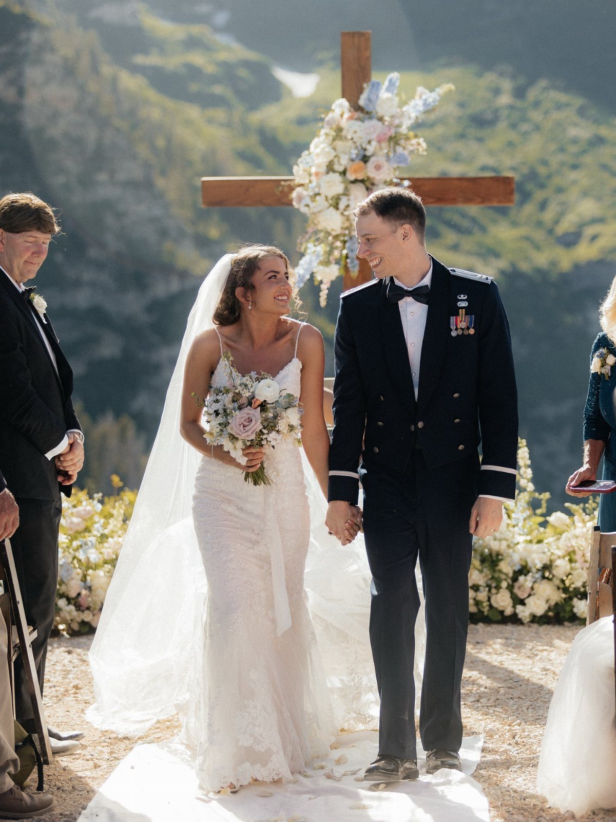 Bride and groom in military uniform walking together at a mountain wedding ceremony.