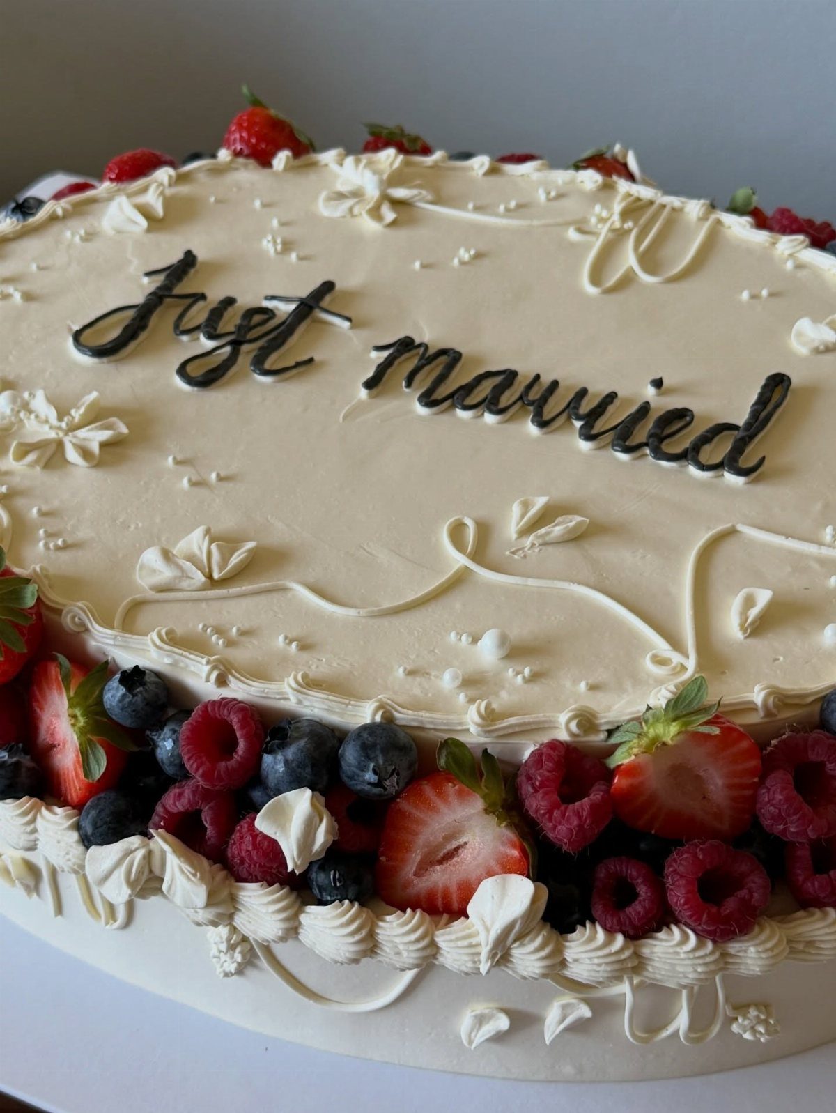 White wedding cake with fresh berries and Just married written in black icing.