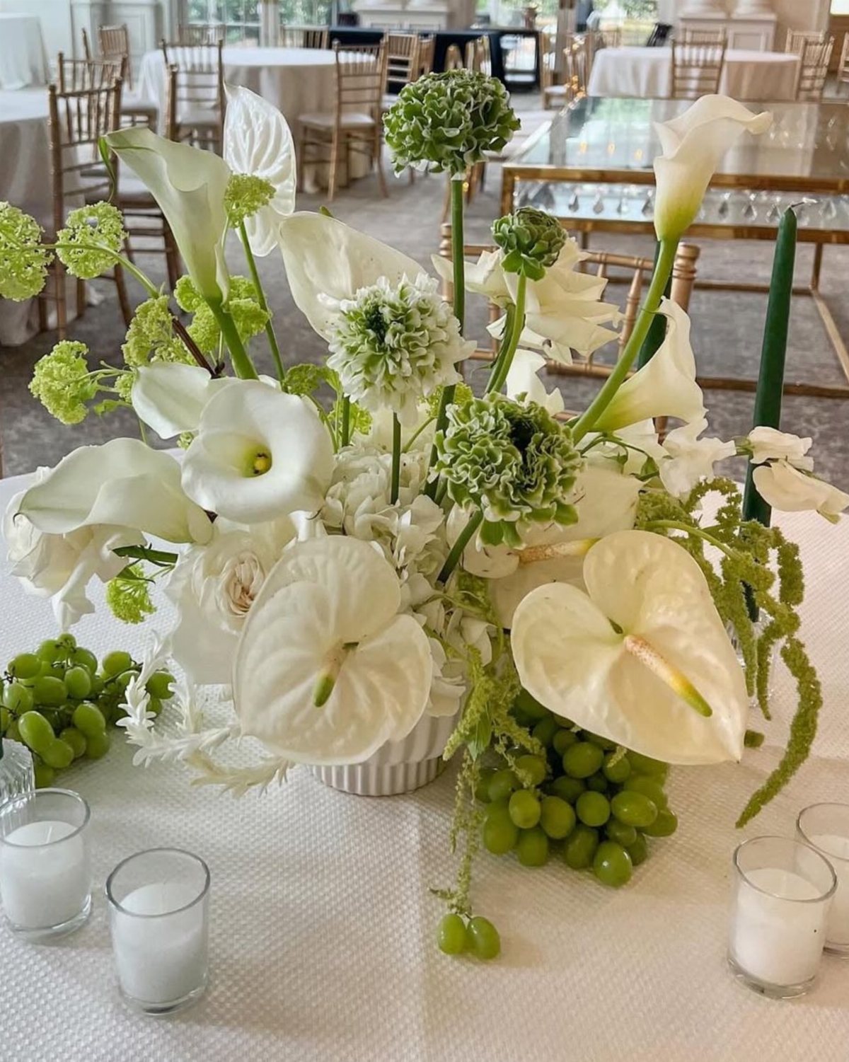 White floral centerpiece with calla lilies and green grapes on a wedding table.