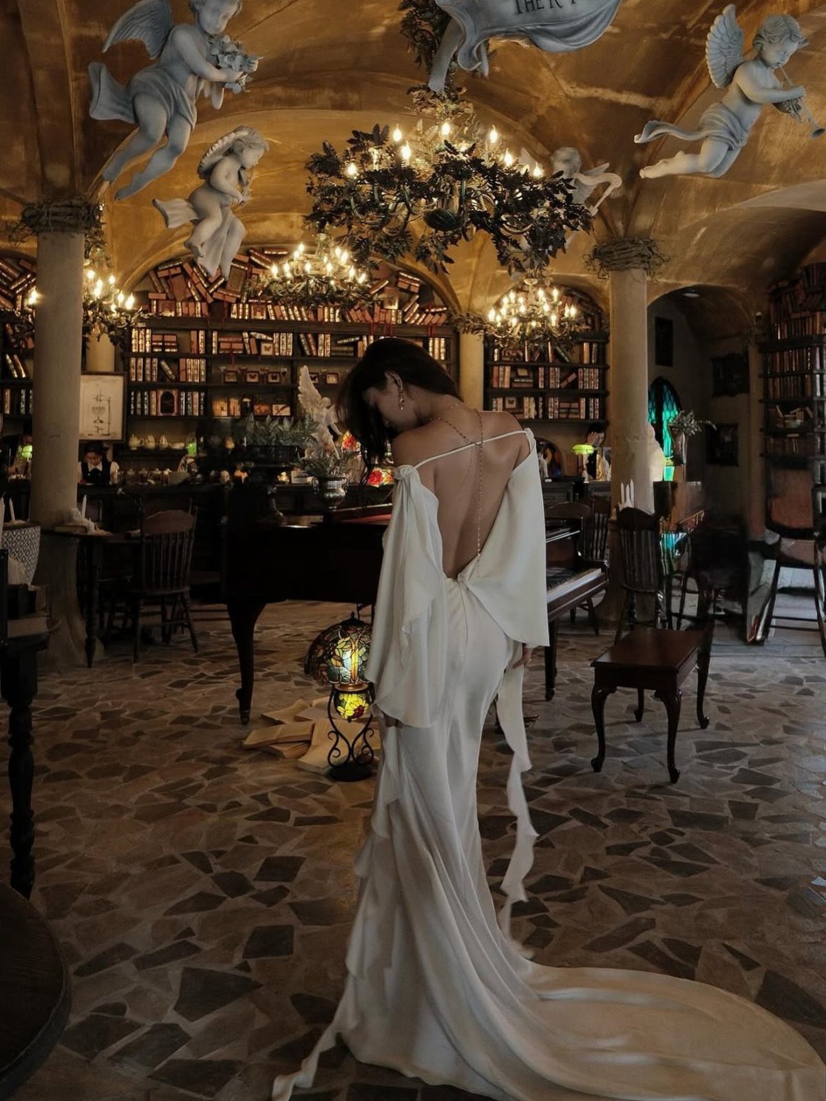 Woman in a backless white silk wedding dress standing in an ornate library