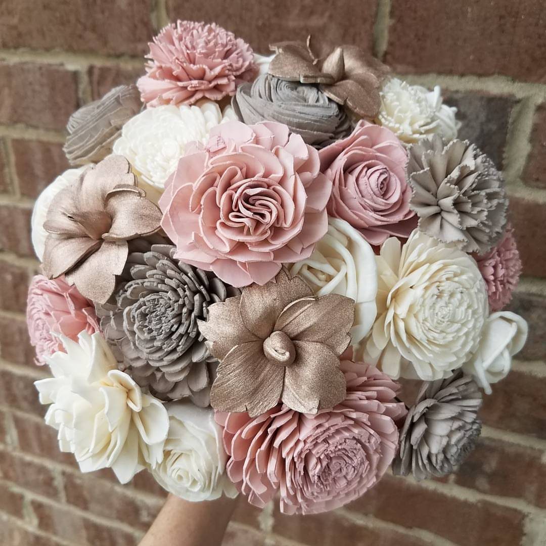 Sola wood flower bouquet in pink, cream, and gold held against brick wall.