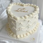 A heart-shaped white wedding cake with gold 'just married' lettering and cream piping.