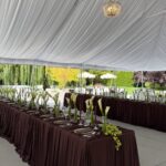 Long banquet tables with dark brown pleated linens and white calla lily centerpieces under a white tent.