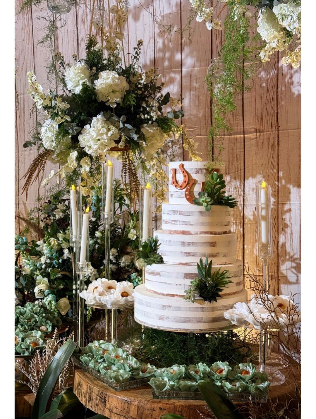A tiered naked wedding cake with a cowboy boot topper surrounded by white flowers and candles.