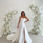 Woman in a strapless white satin A-line wedding dress with a high leg slit.
