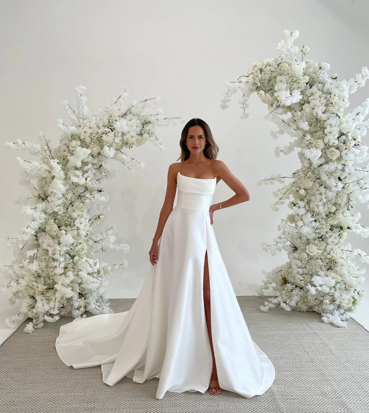 Woman in a strapless white satin A-line wedding dress with a high leg slit.