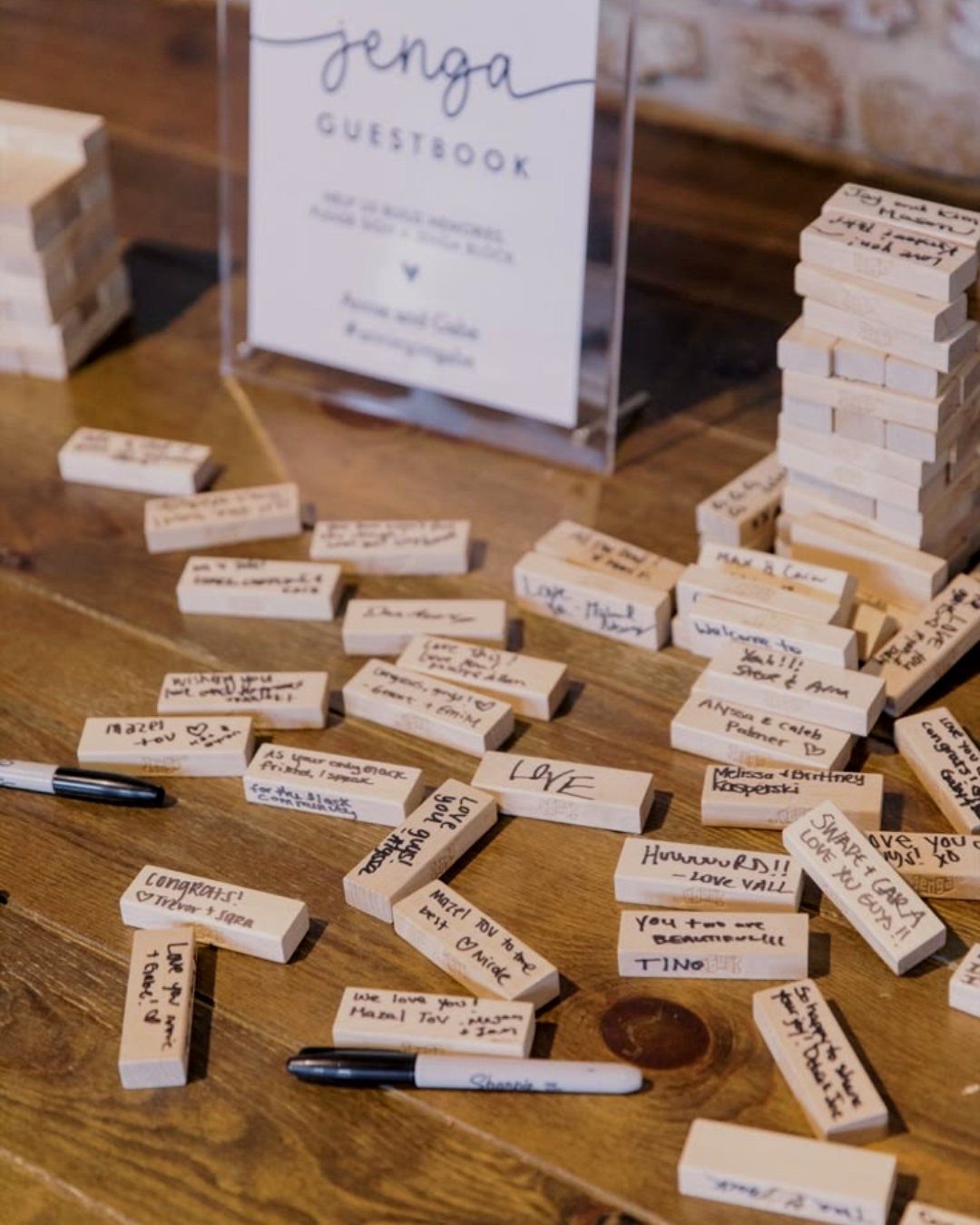 Wooden Jenga blocks with handwritten guest messages on a rustic wooden table.