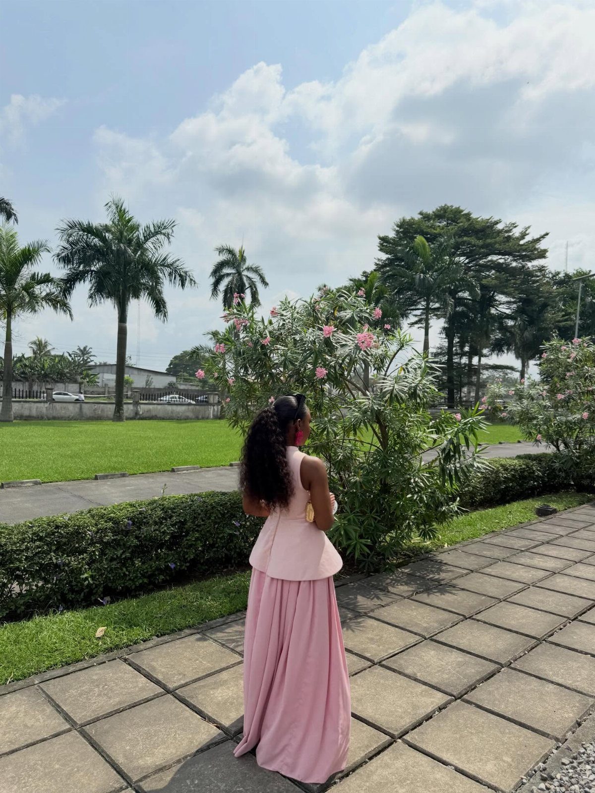 Woman in a long light pink sleeveless gown standing on a garden path