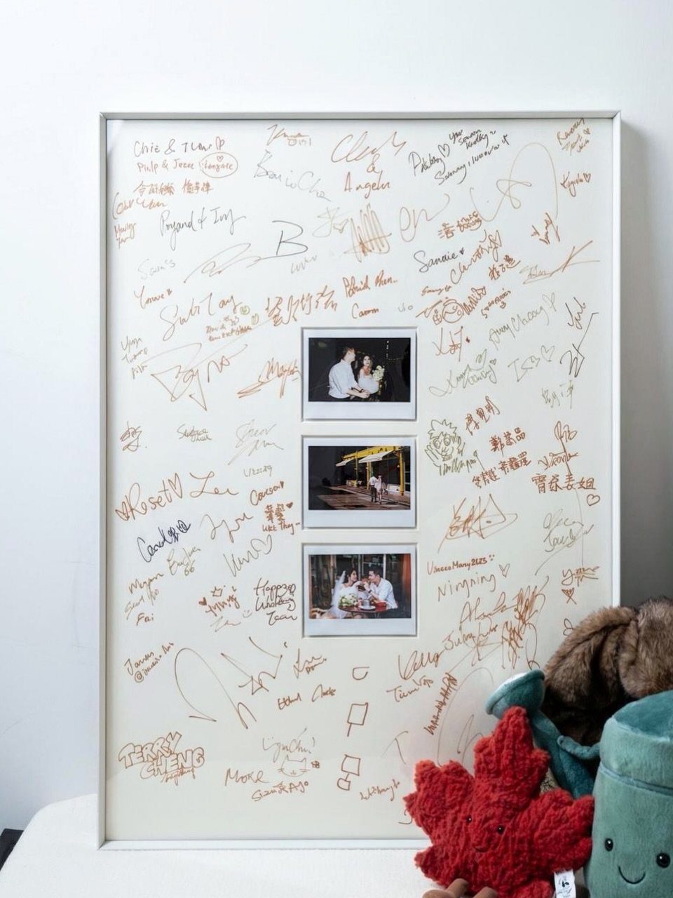 Framed wedding guest sign in board with handwritten signatures and three polaroid photos.