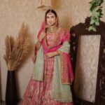 A woman wearing an ornate pink and green traditional Indian bridal lehenga and jewelry.