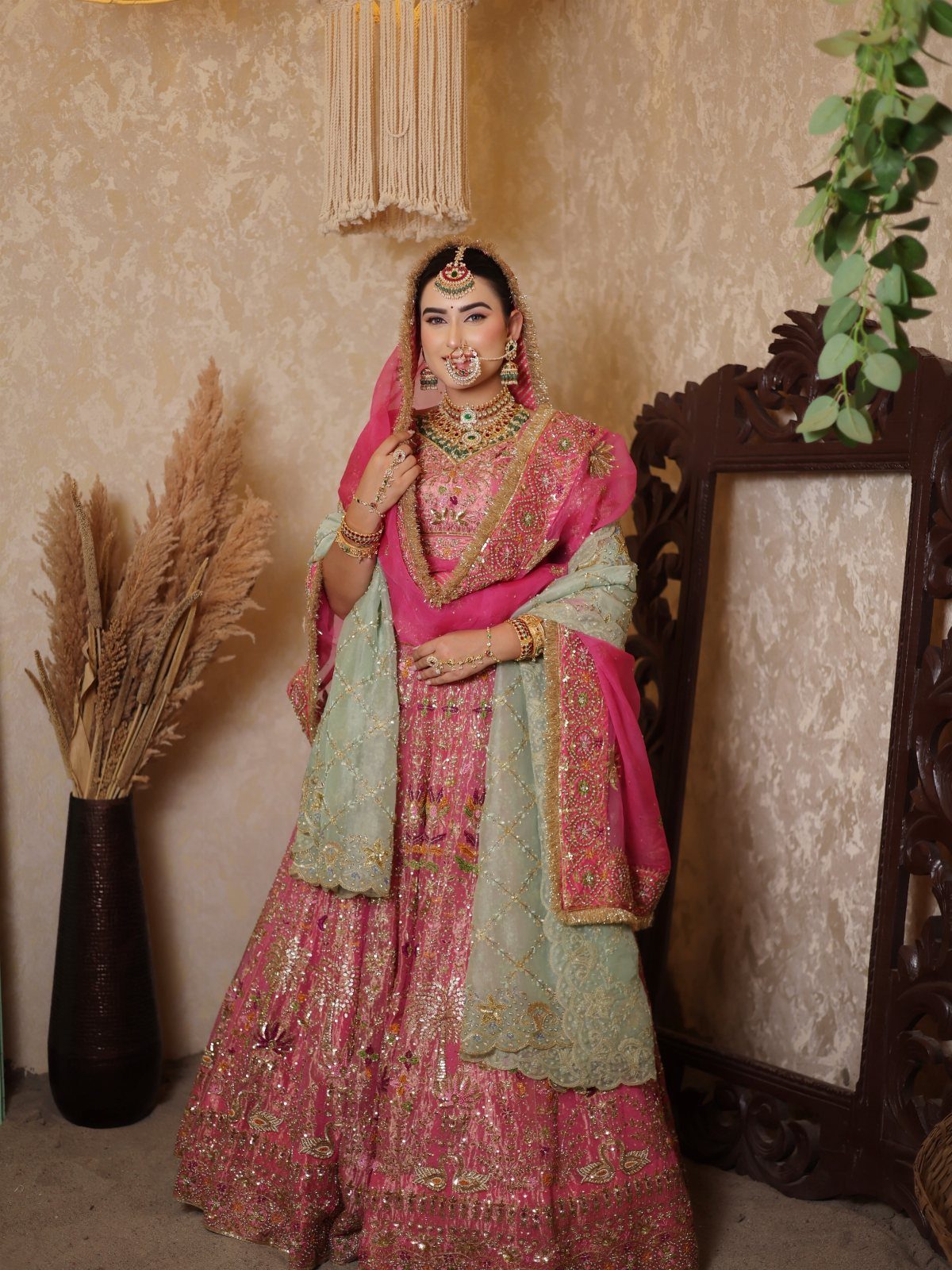 A woman wearing an ornate pink and green traditional Indian bridal lehenga and jewelry.