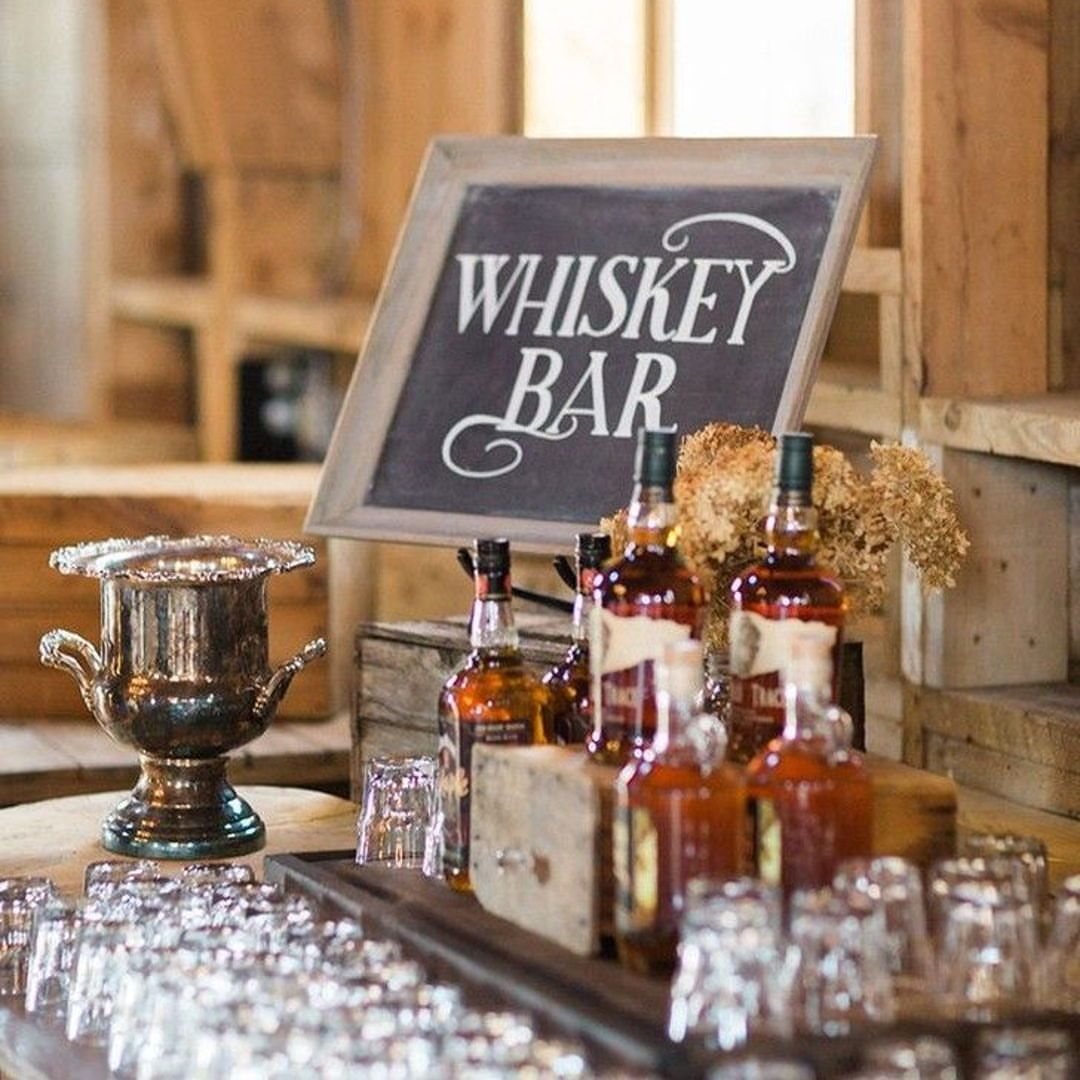 Whiskey bottles and glasses arranged on a table next to a whiskey bar chalkboard sign.