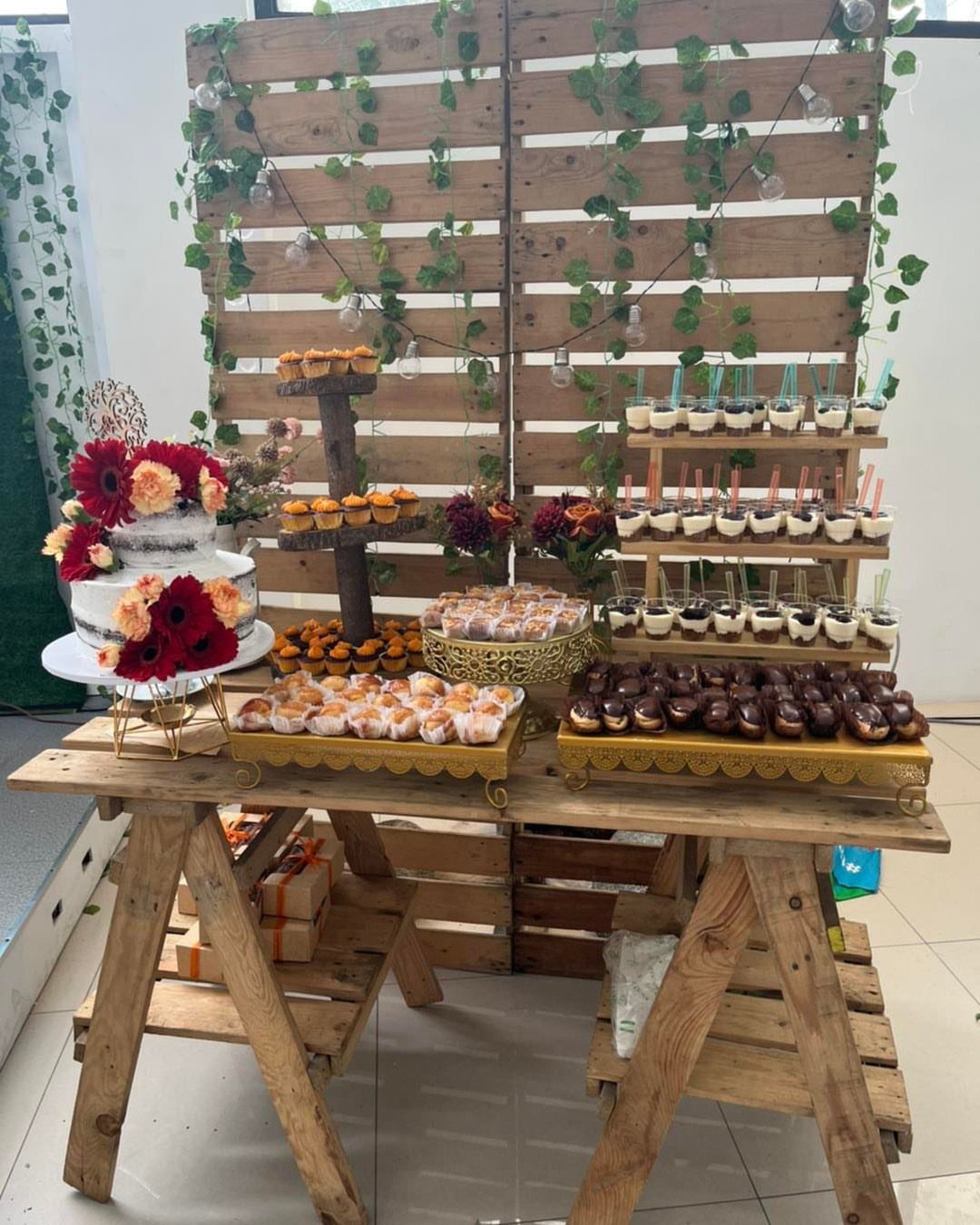 A dessert table with a white floral cake and various pastries on a rustic wooden trestle.