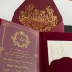 Burgundy wedding invitation with gold foil damask patterns and elegant calligraphy on a white card.