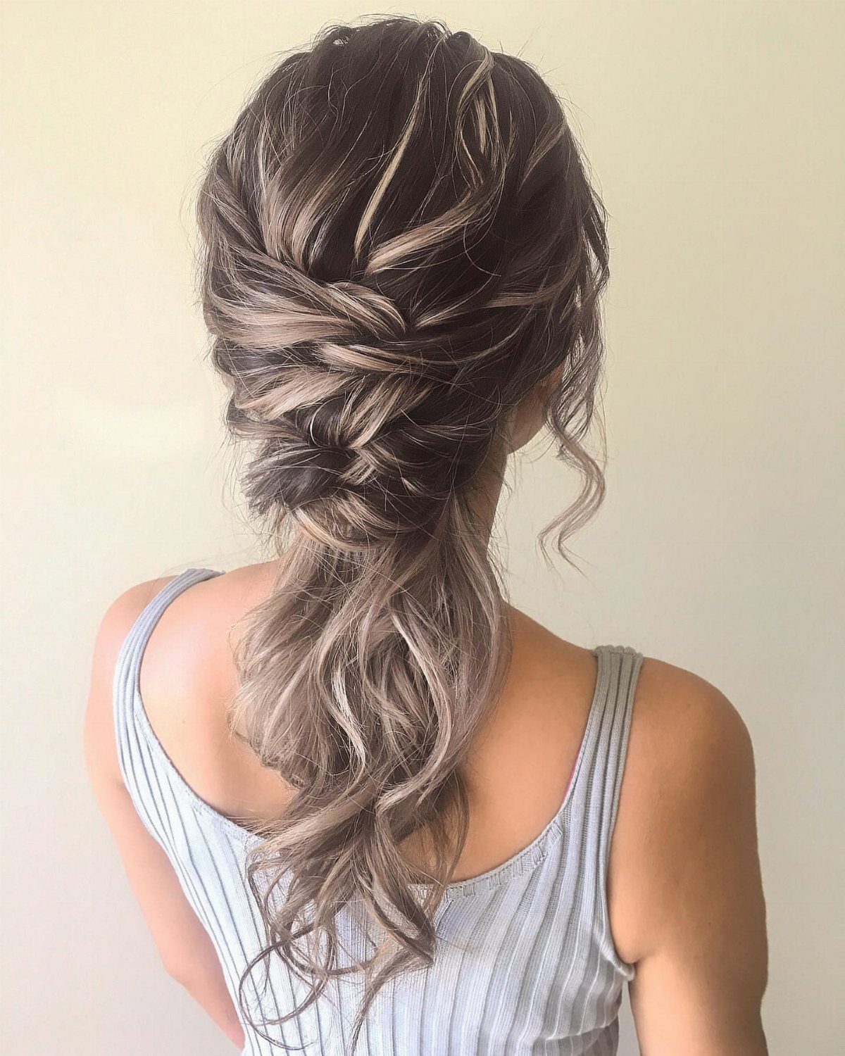 Voluminous low ponytail with curls and twisted braids on brown highlighted hair.