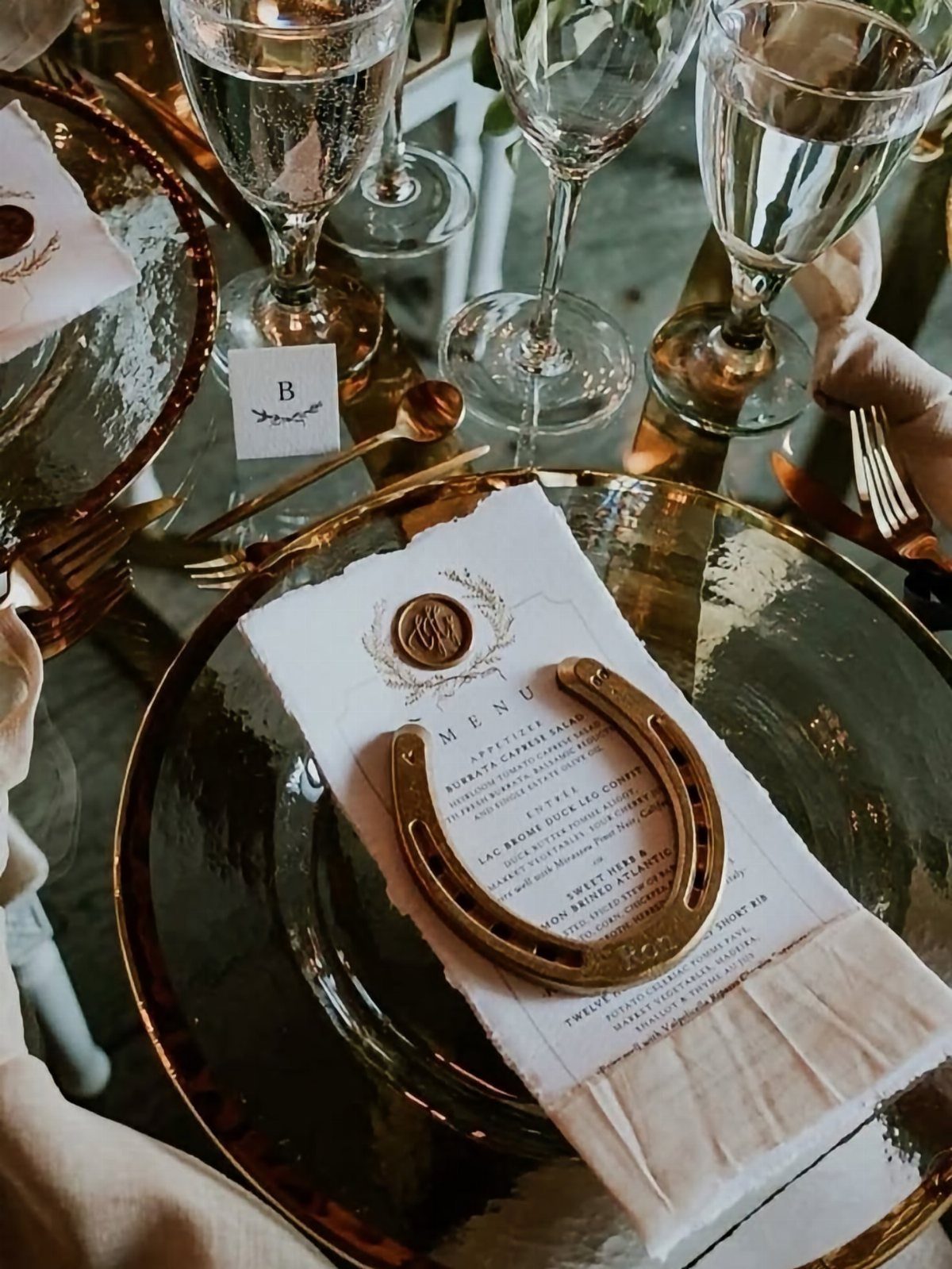 Wedding table setting with a gold horseshoe on a menu and gold-rimmed plates.