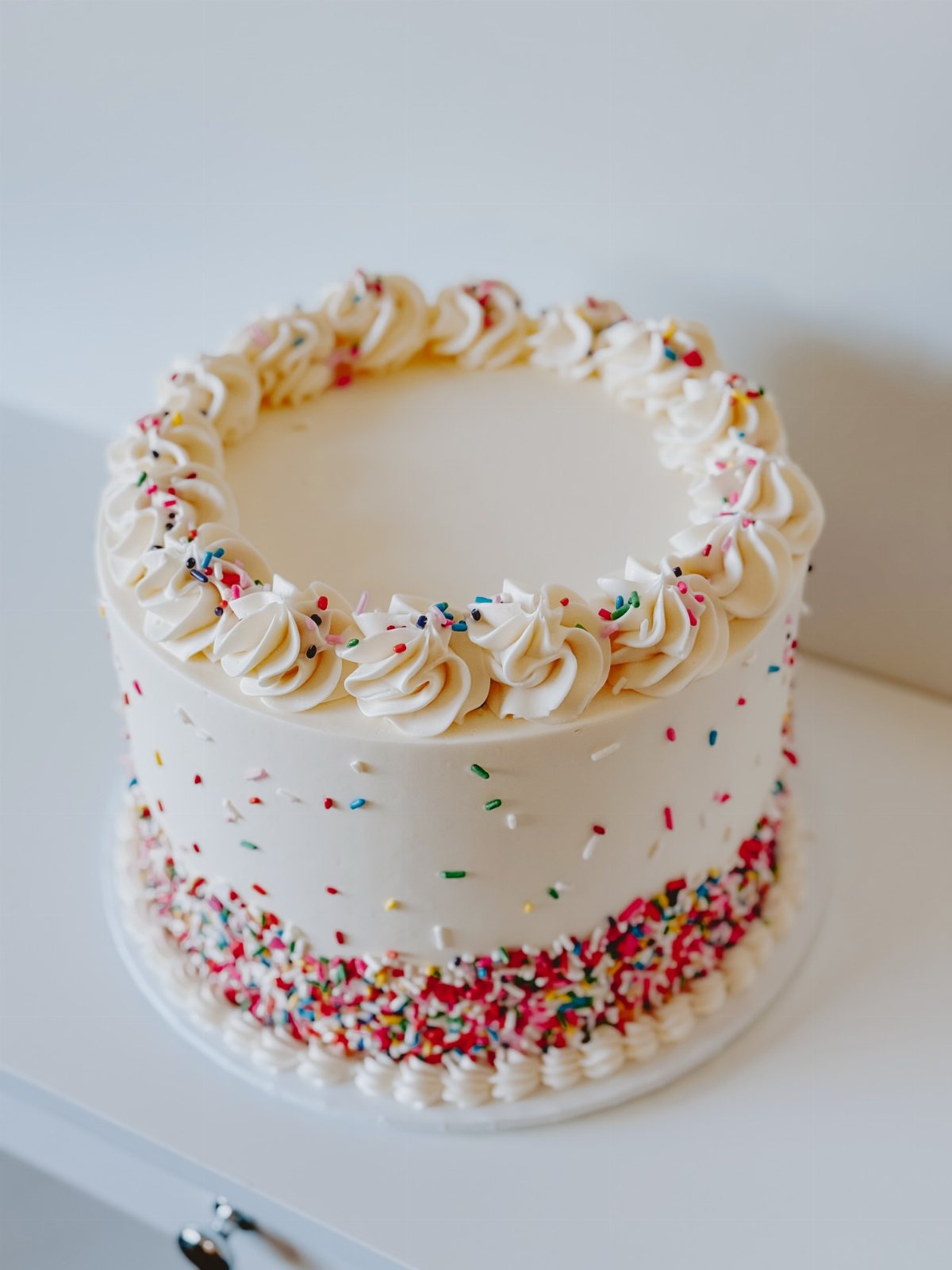 A white buttercream cake decorated with colorful sprinkles around the base and sides.